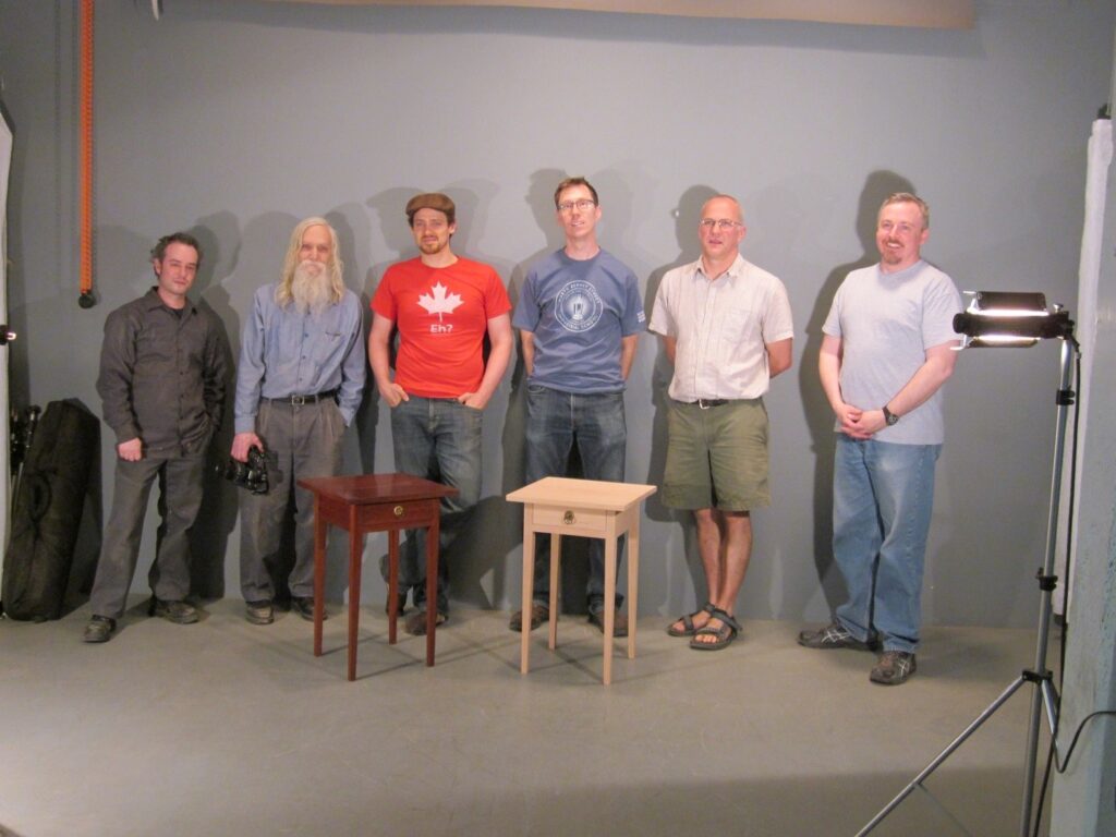 The group of furniture making students and Instructor Lance Patterson (second from left) at the Houghton Library with the completed reproduction and original tables.