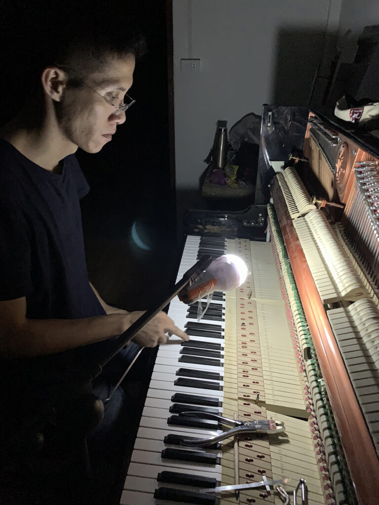 Shin tunes a piano in the dark