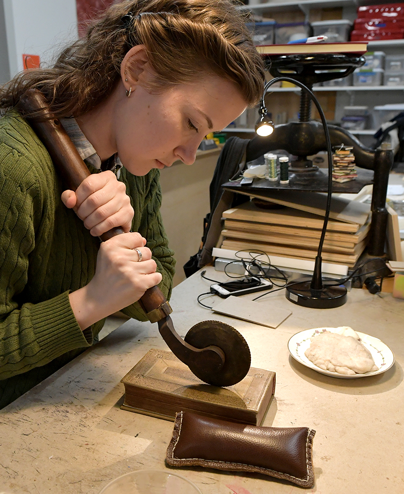 Bookbinding student tooling a book cover