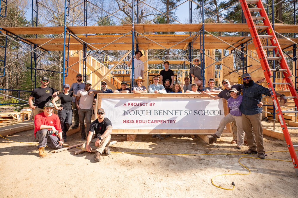 Carpentry students pose with a sign saying "A Project by North Bennet Street School"