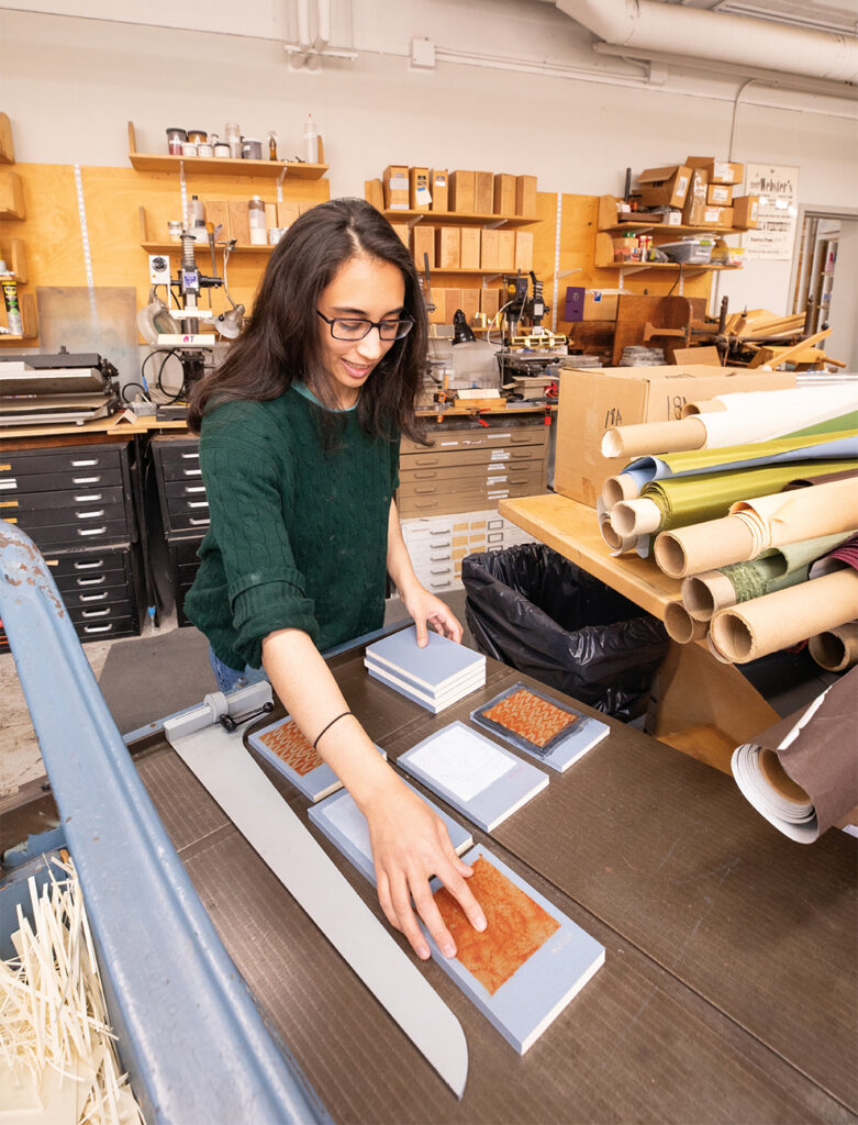 India arranging her books on the board shear in the Bookbinding space