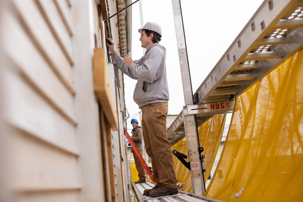 Memorial Hall under construction in spring 2022 - student working on the siding on the upper story