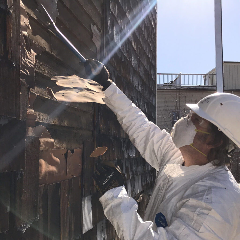 Student removing exterior paint from the siding