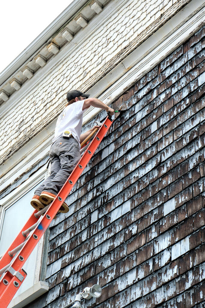 Student on a ladder inspecting the exterior shingles in spring 2020