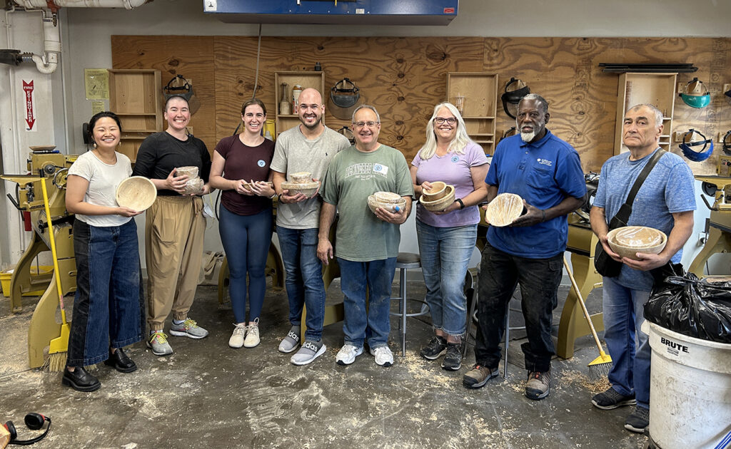 8 Students in a bowl turning class pose with their bowls