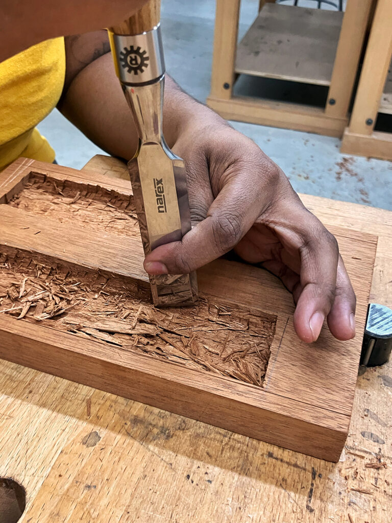 Student using a chisel to cut wood from inside an oilstone box