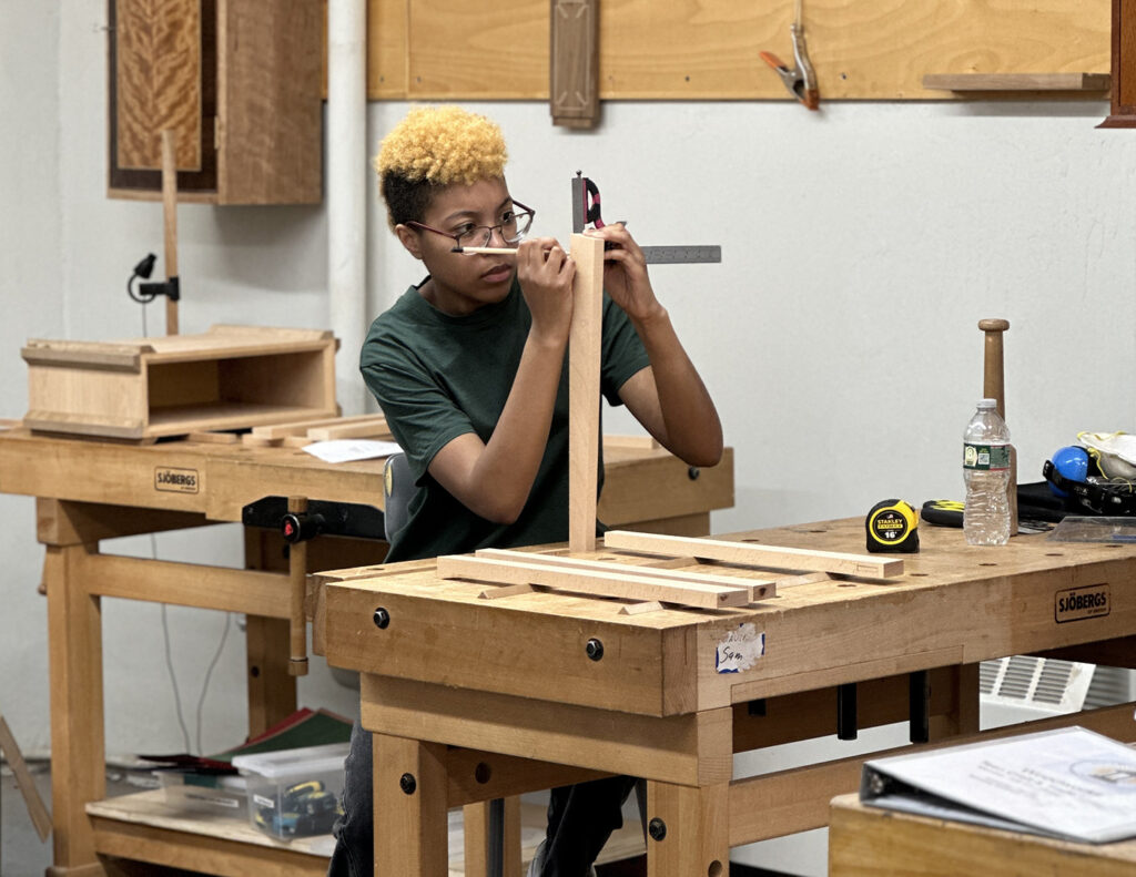 Woodworking intensive student Gabby measures a piece of wood