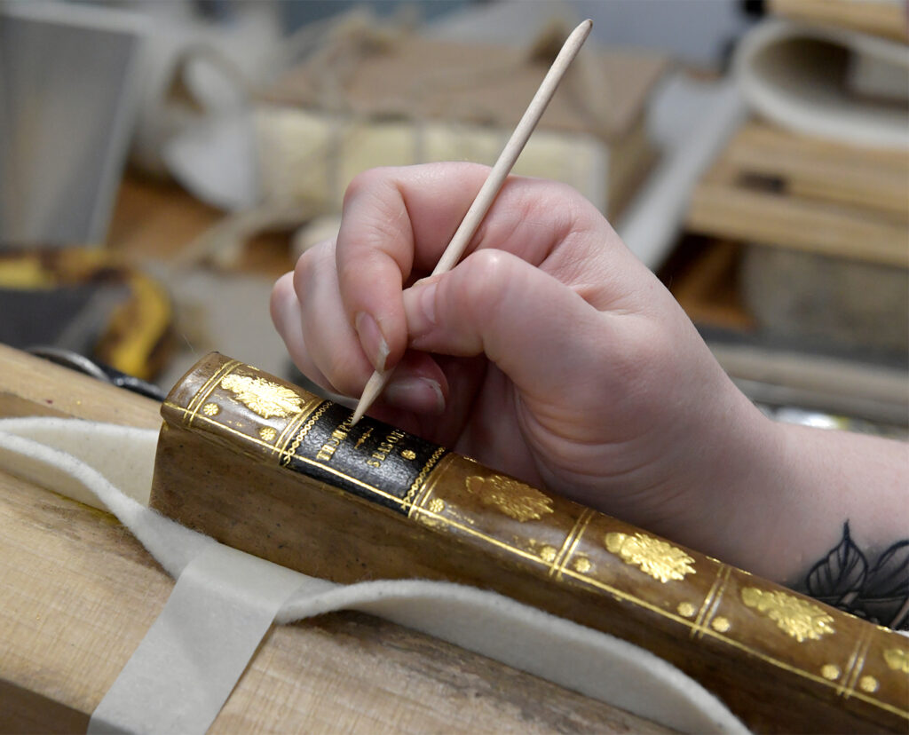 Student applying gold tooling to a spine