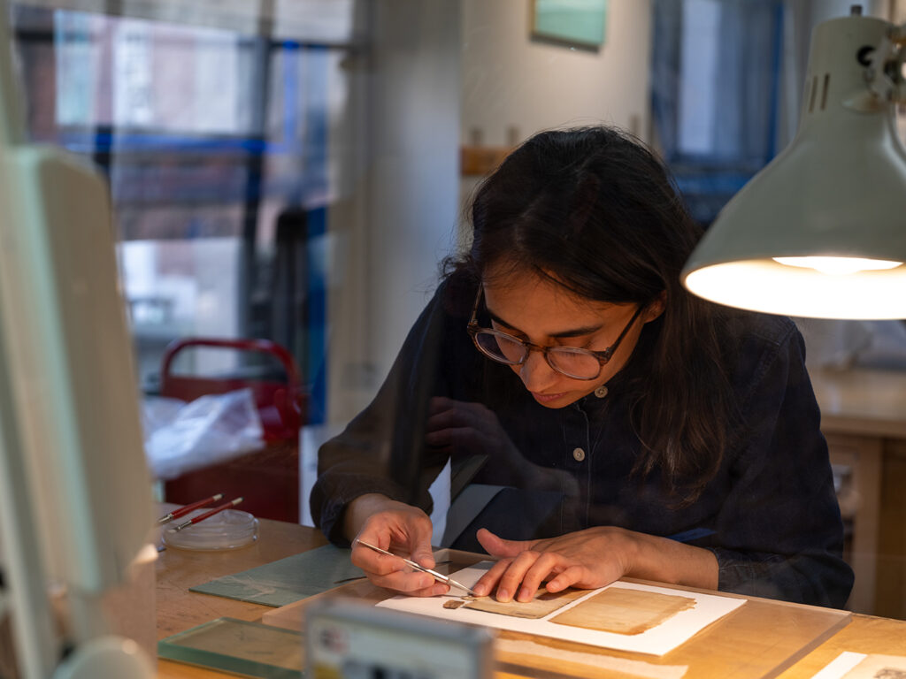 Former fellow India Patel at work on a treatment of an 1833 O-jib-ue Spelling Book.