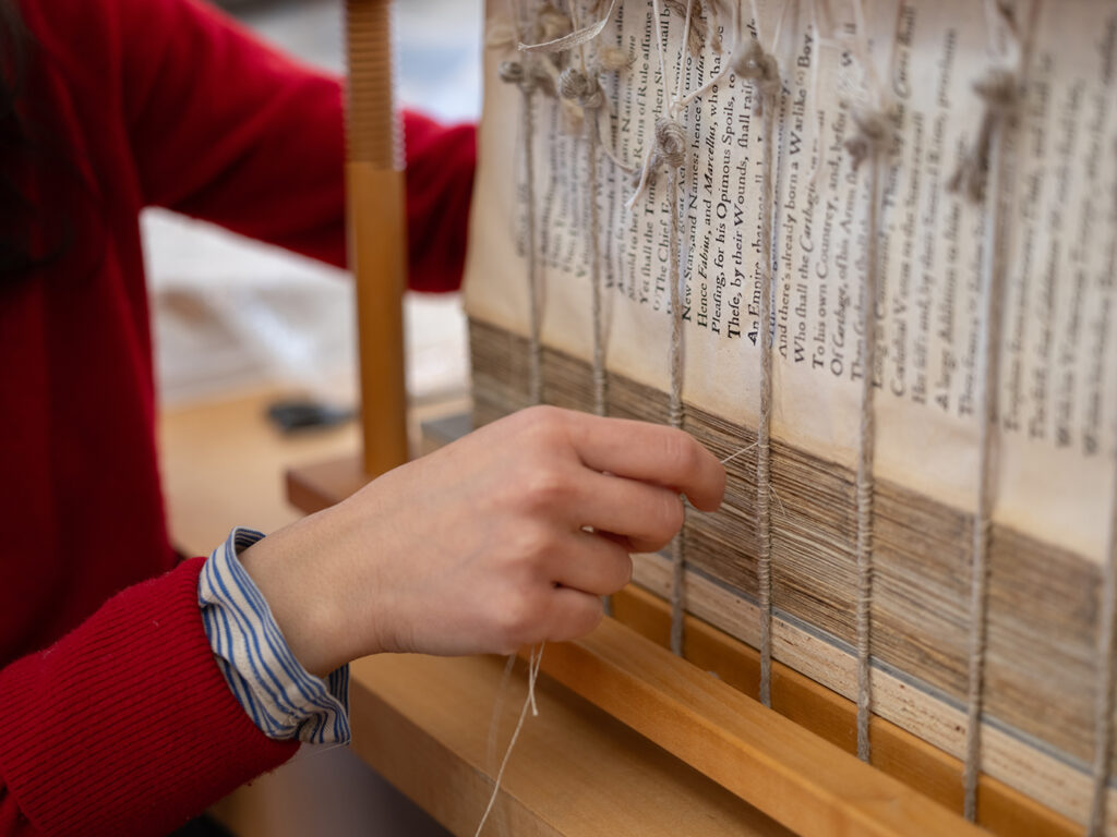 Former fellow India Patel resewing a book, The Second Punick War Between Hannibal, and the Romanes, as part of a conservation treatment.