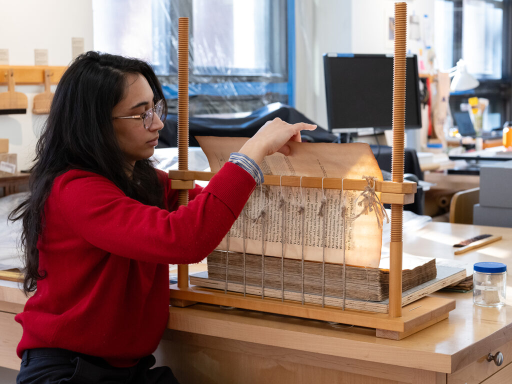 Former fellow India Patel resewing a book, The Second Punick war between Hannibal, and the Romanes, as part of a conservation treatment.